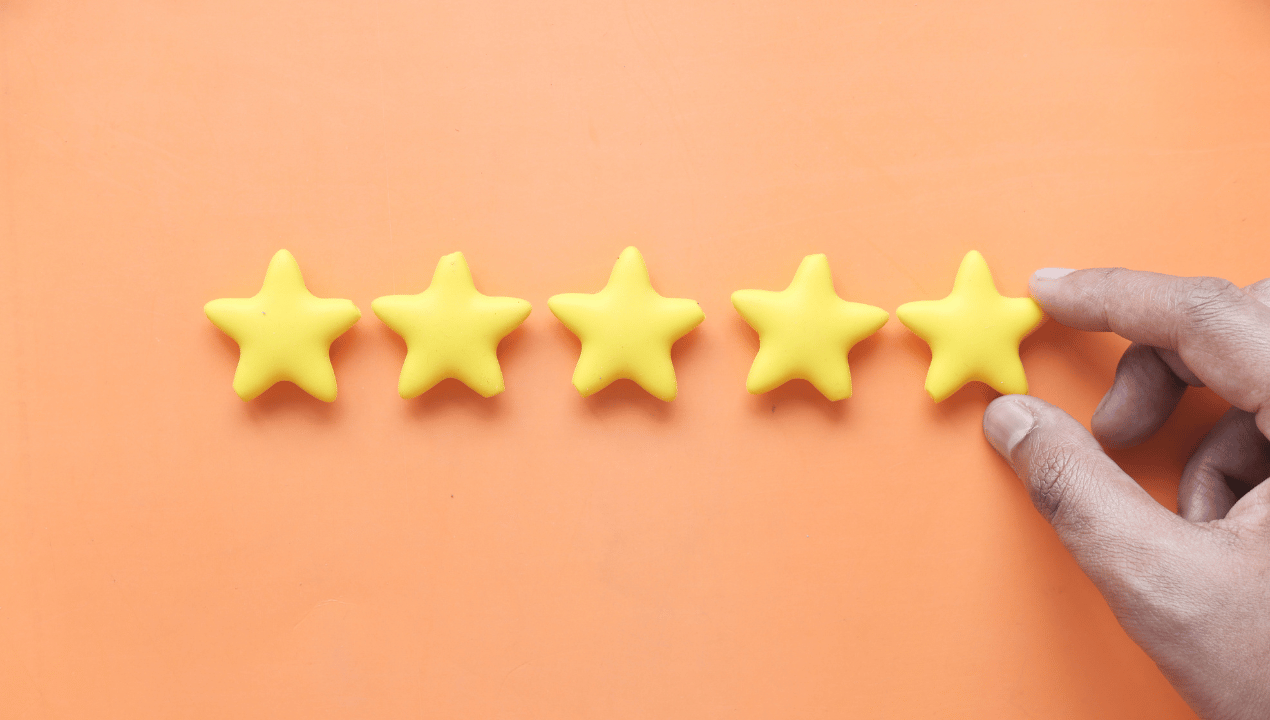 A hand placing the fifth of five yellow star shapes in a row on an orange background