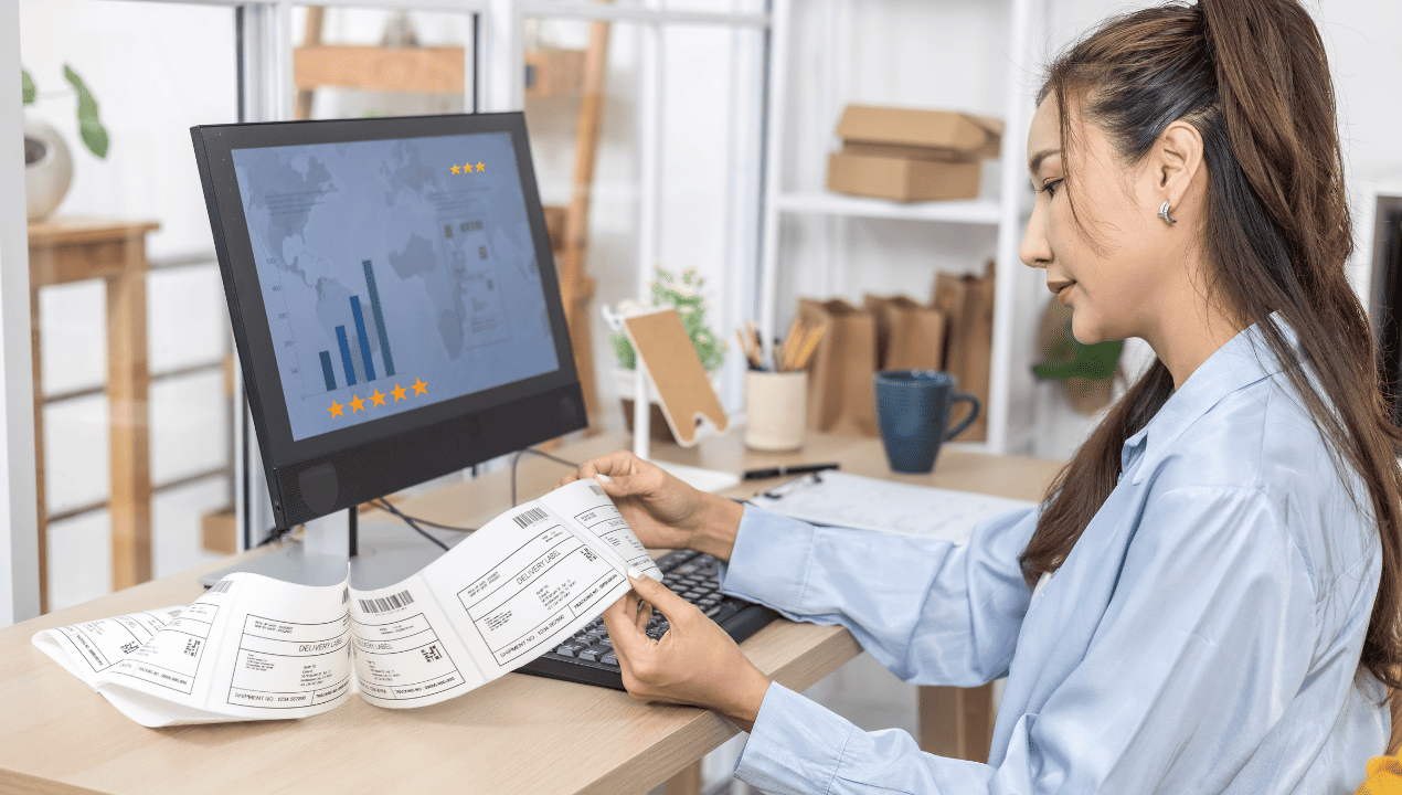 A business owner reviewing paperwork beside a monitor displaying business ratings and analytics