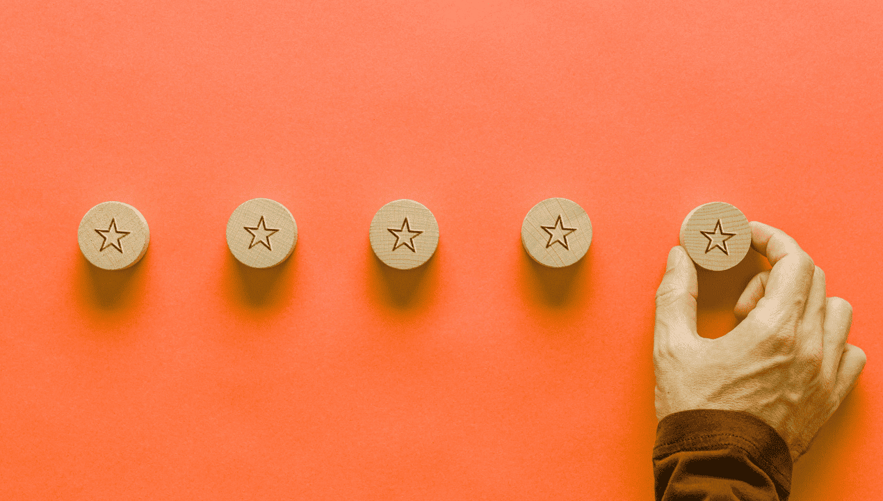 A hand placing the fifth star in a row of wooden review stars against an orange background